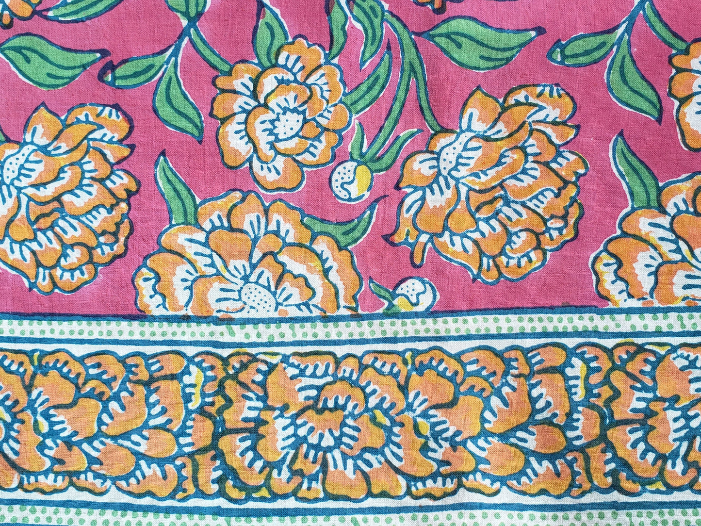 Detalle de sobrecama 100% algodón estampado a mano, base rosa con flores naranjas y tallos verdes. Hecho en la India.