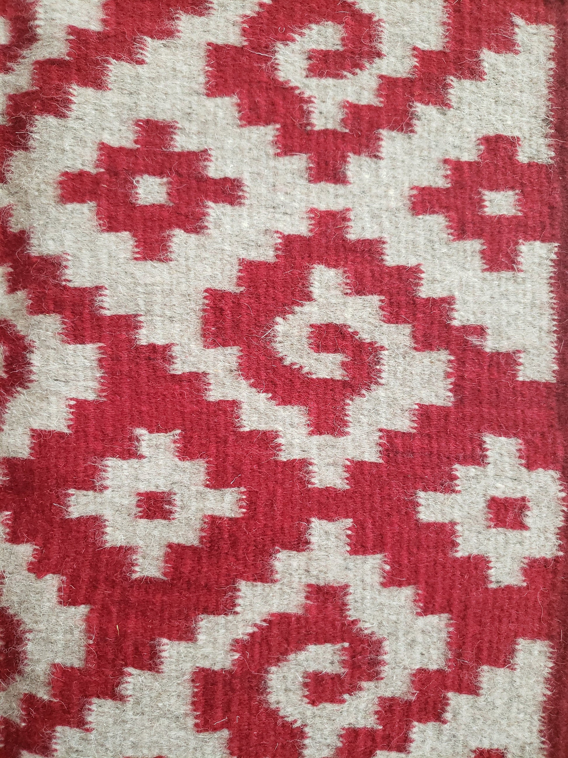 Detalle de tapete mexicano, tejido en telar y teñido artesanalmente. Diseño geométrico con grecas color rojo, tinte natural de grana cochinilla.