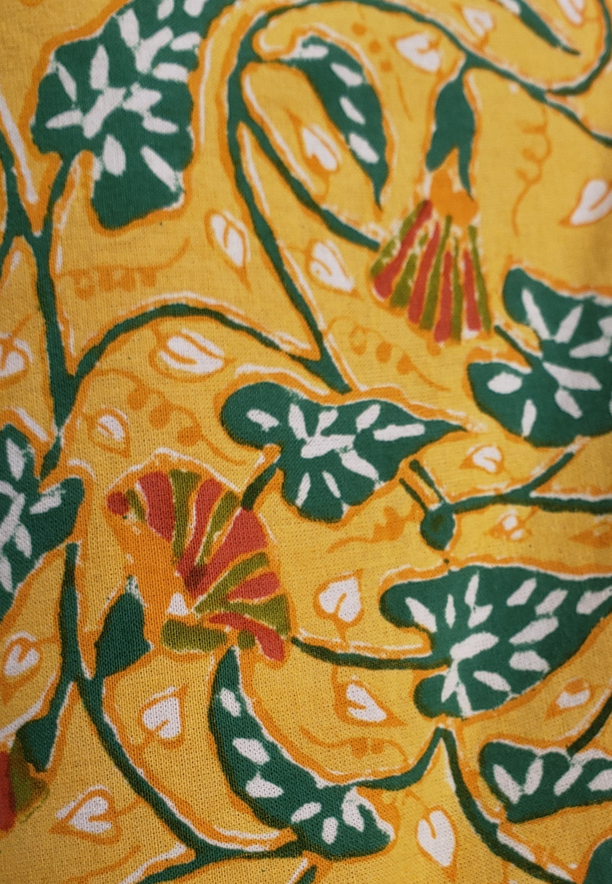 Detalle de estampado a mano, base amarilla con flores naranjas y tallos y hojas verdes.