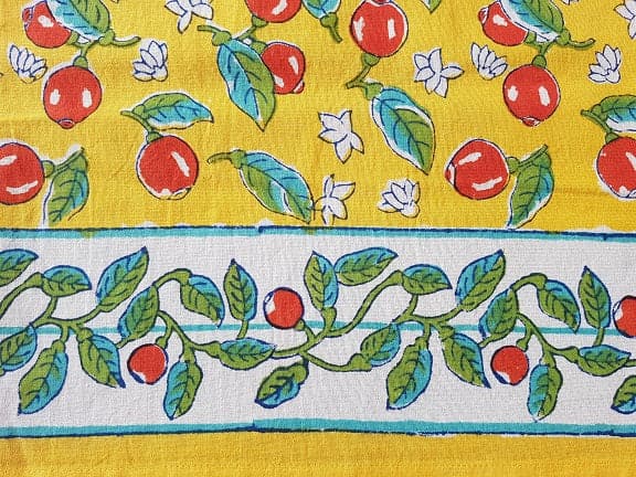 Mantel rectangular amarillo estampado a mano con cerezas y borde blanco con hojas y cerezas.