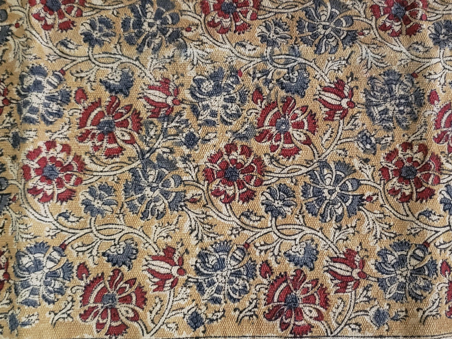 Detalle de tapete algodón estampado a mano con diseño tradicional Kalamkari, base ocre con diseño floral en tonos tierra. Hecho en la India.