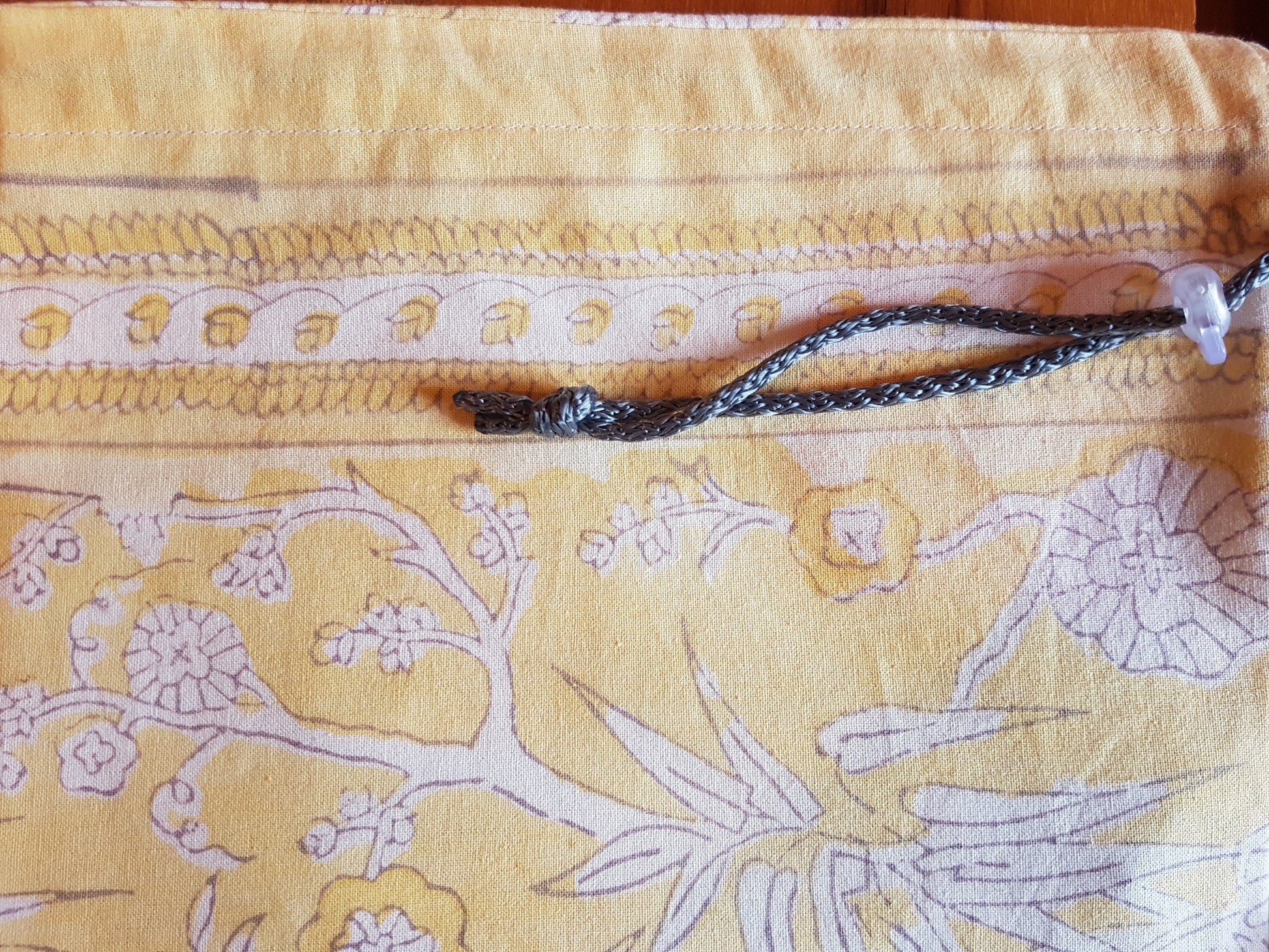 Detalle de jareta gris en funda para tapete de yoga 100% algodón, estampada a mano amarilla vegetación y pájaros en color gris con blanco. Hecha en la India.