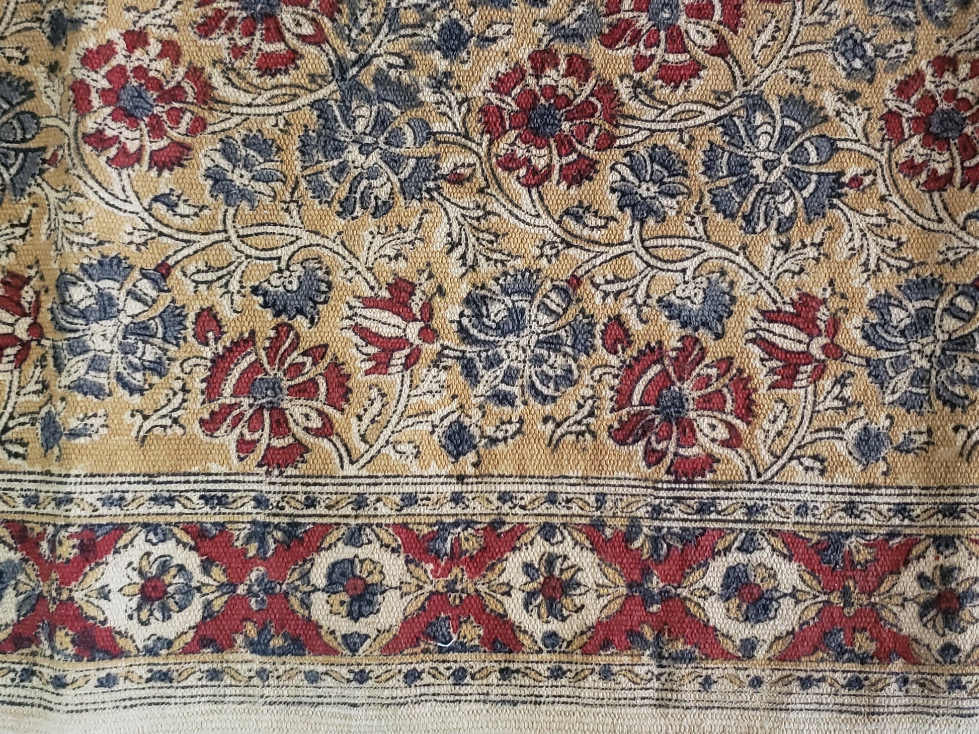 Detalle de tapete 100% algodón estampado a mano con diseño tradicional Kalamkari, base ocre con diseño floral en tonos tierra. Hecho en la India.