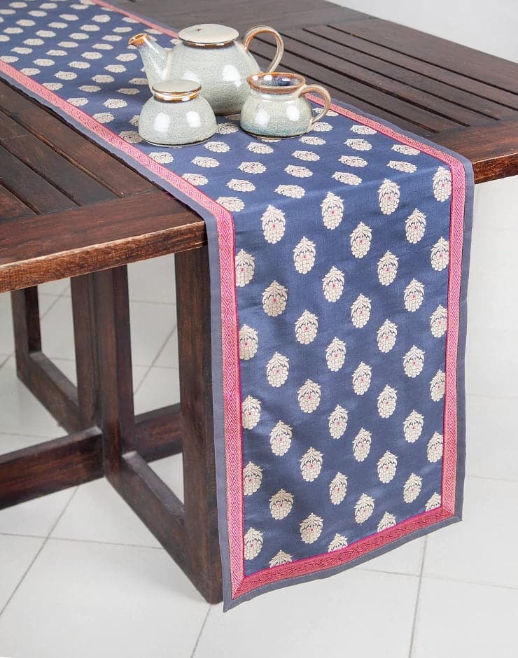 Camino de mesa en seda gris con bordes en tono rosa tornasol y flores entre tejidas con hilo dorado. Hecho en la India.
