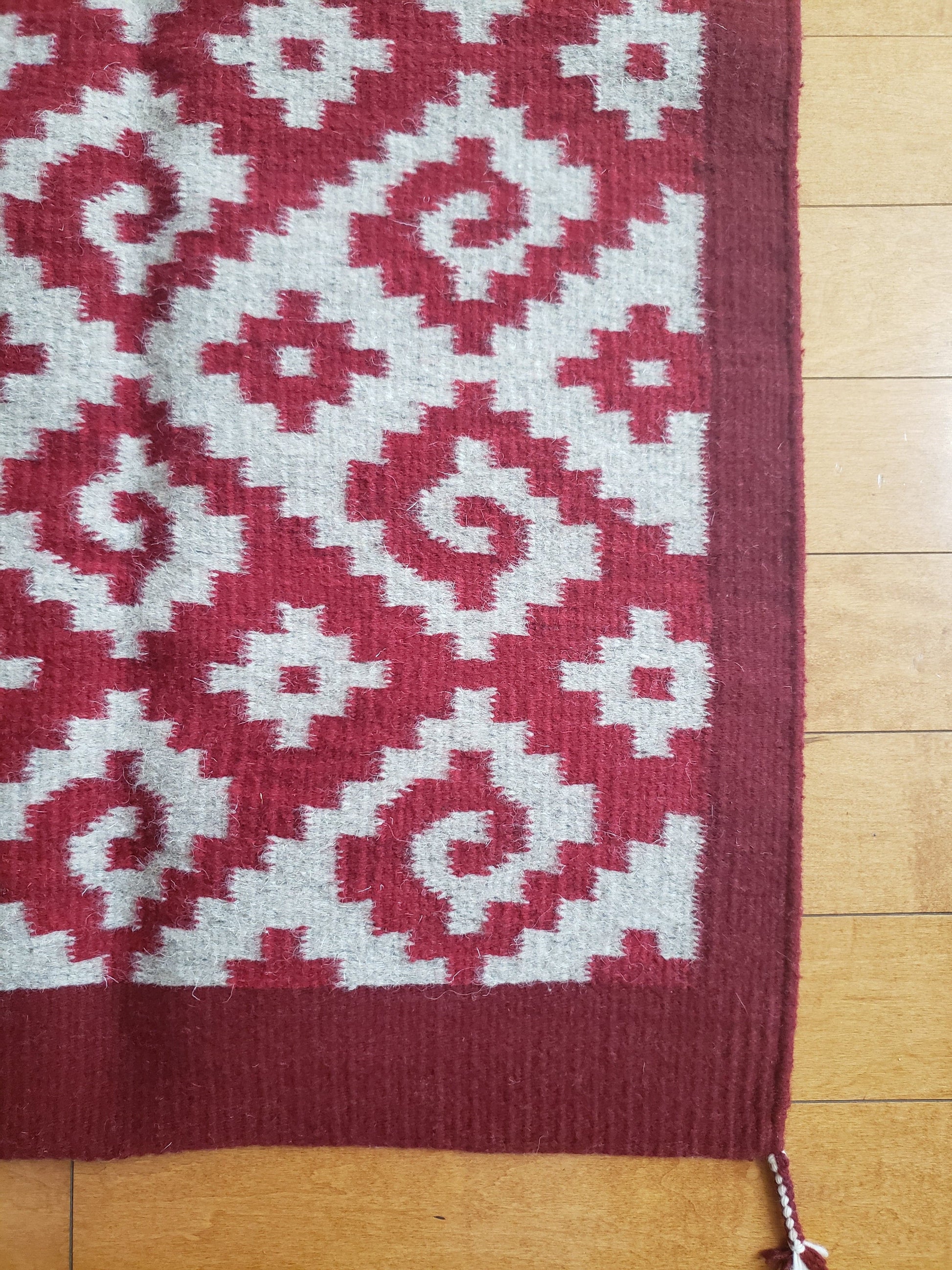 Detalle de tapete mexicano, tejido en telar y teñido artesanalmente. Diseño geométrico con grecas color rojo, tinte natural de grana cochinilla.